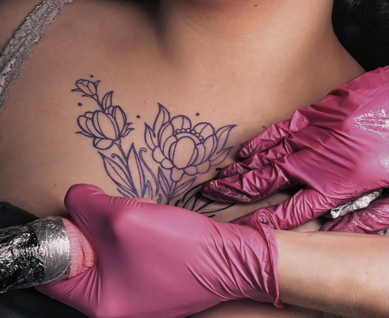 Pretty Pricks artist in pink gloves stencilling a floral chest tattoo